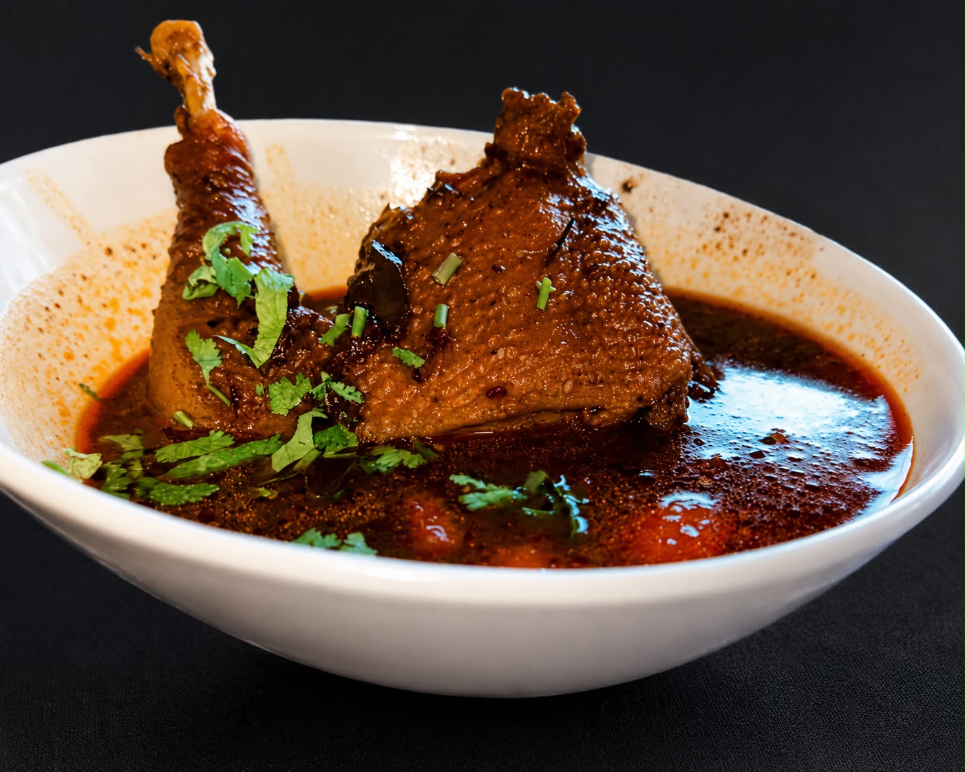 Gallina india en caldo oscuro servida en plato hondo